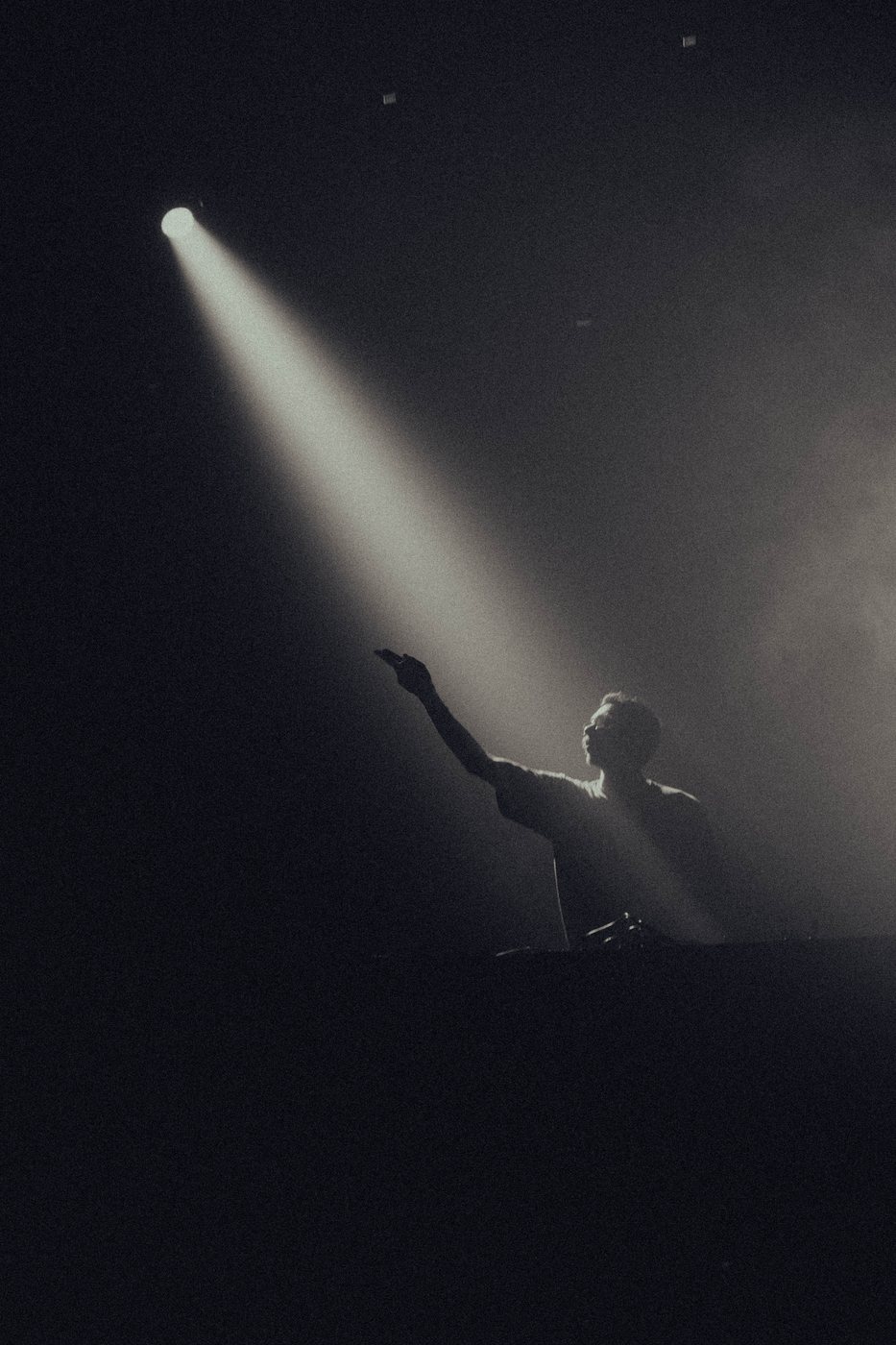 Silhueta de DJ contra feixe de luz vertical em meio à fumaça de palco