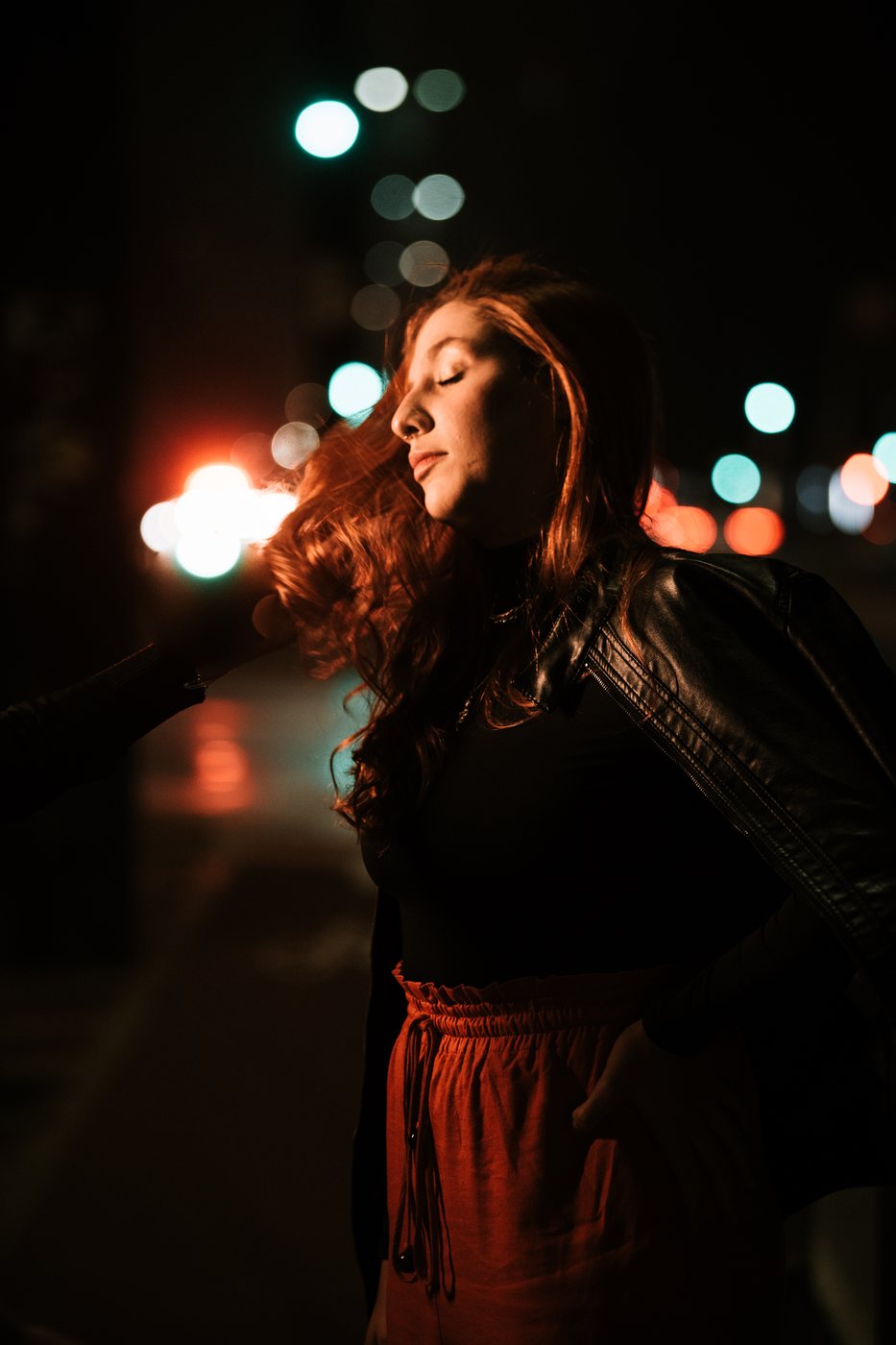 Retrato com cabelo ao vento e luz de contorno quente contra bokeh de luzes noturnas